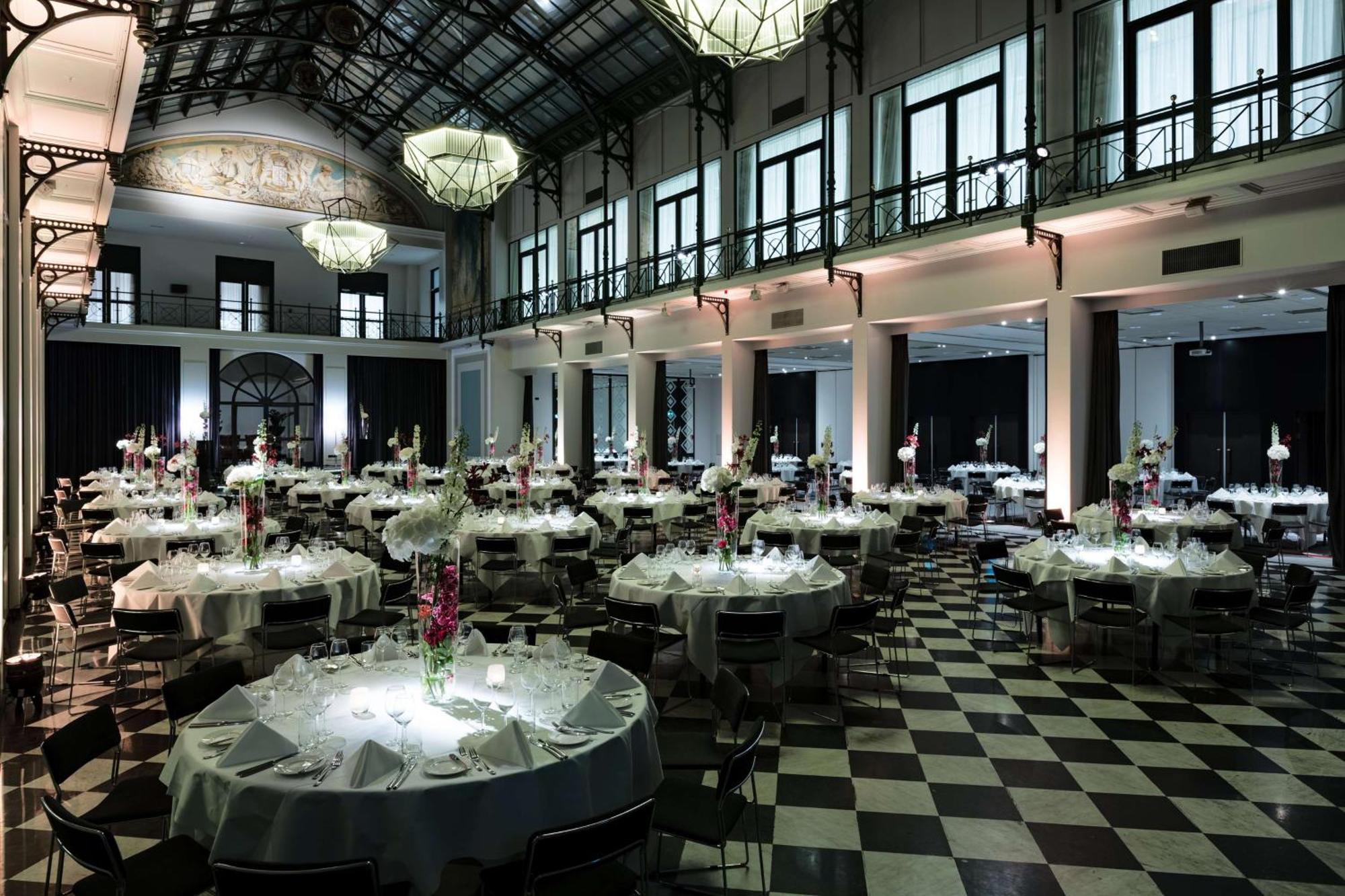 Anantara Grand Hotel Krasnapolsky Amsterdam Buitenkant foto The photo shows an elegant banquet hall set up for an event. The space features numerous round tables, each dressed with white tablecloths and decorated with floral centerpieces. The room has high ceilings with large chandeliers hanging from them and