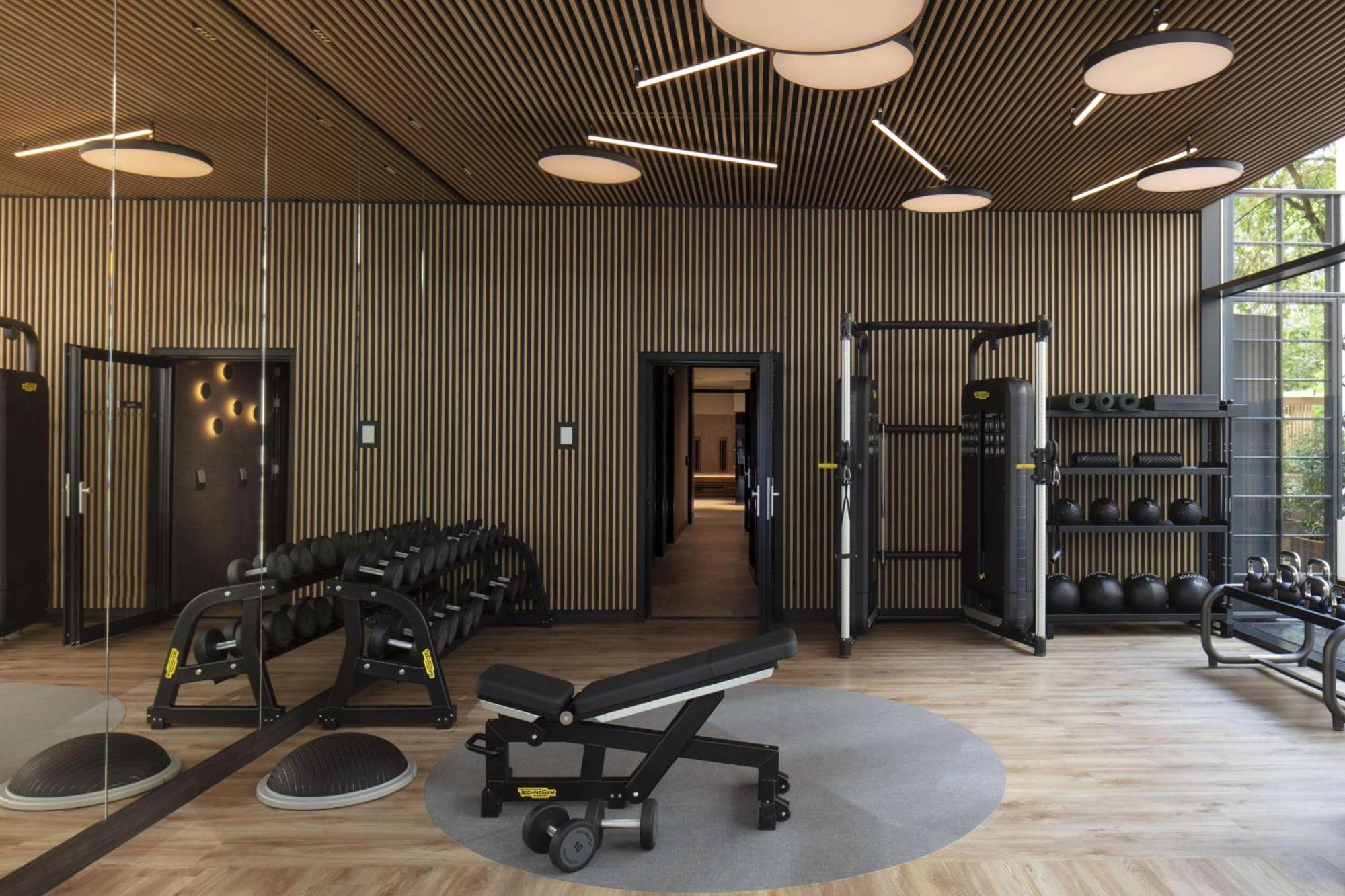 Anantara Grand Hotel Krasnapolsky Amsterdam Buitenkant foto The photo shows a modern gym interior. It features wooden paneling on the walls and a wooden floor, giving a warm and contemporary atmosphere. On the left side, there are sets of dumbbells arranged on a rack. In the center, there is a workout bench, 